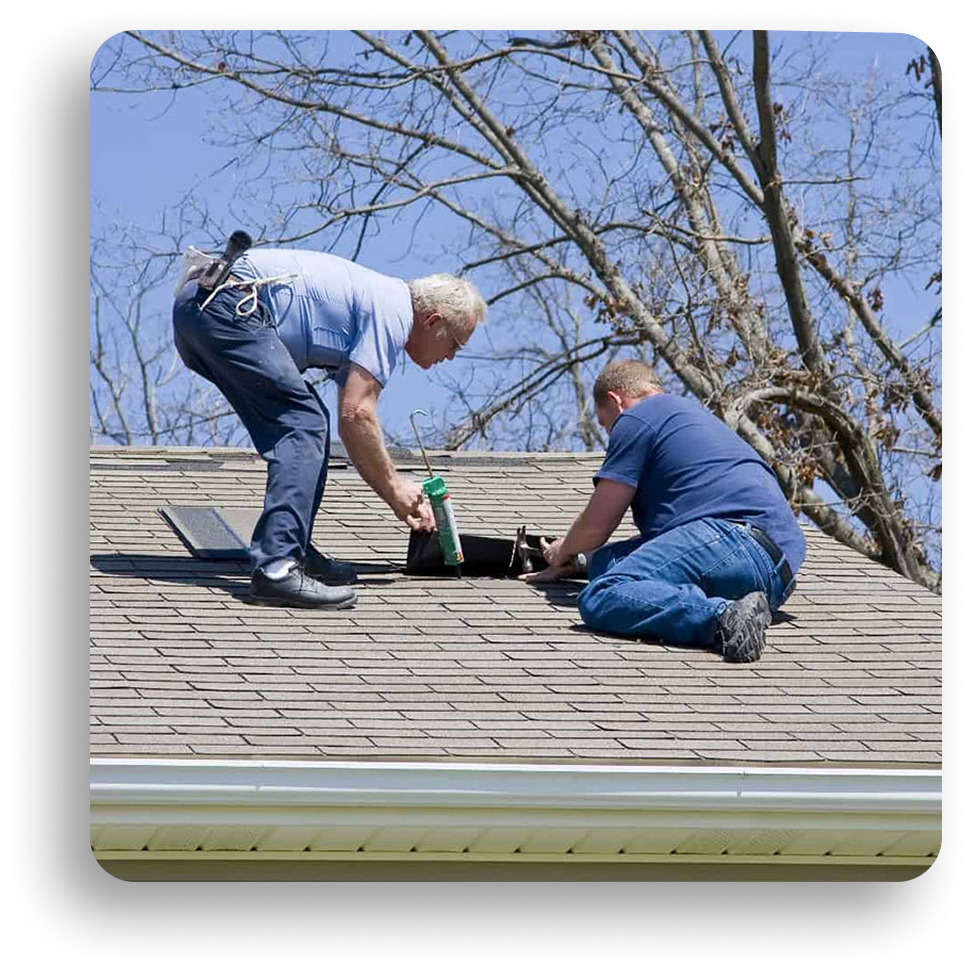 Two people kneel on a shingled roof in North Texas, working together to repair an opening with a caulking gun. Leafless tree branches and a clear blue sky frame this scene from American Patriot Roofing’s expert team.