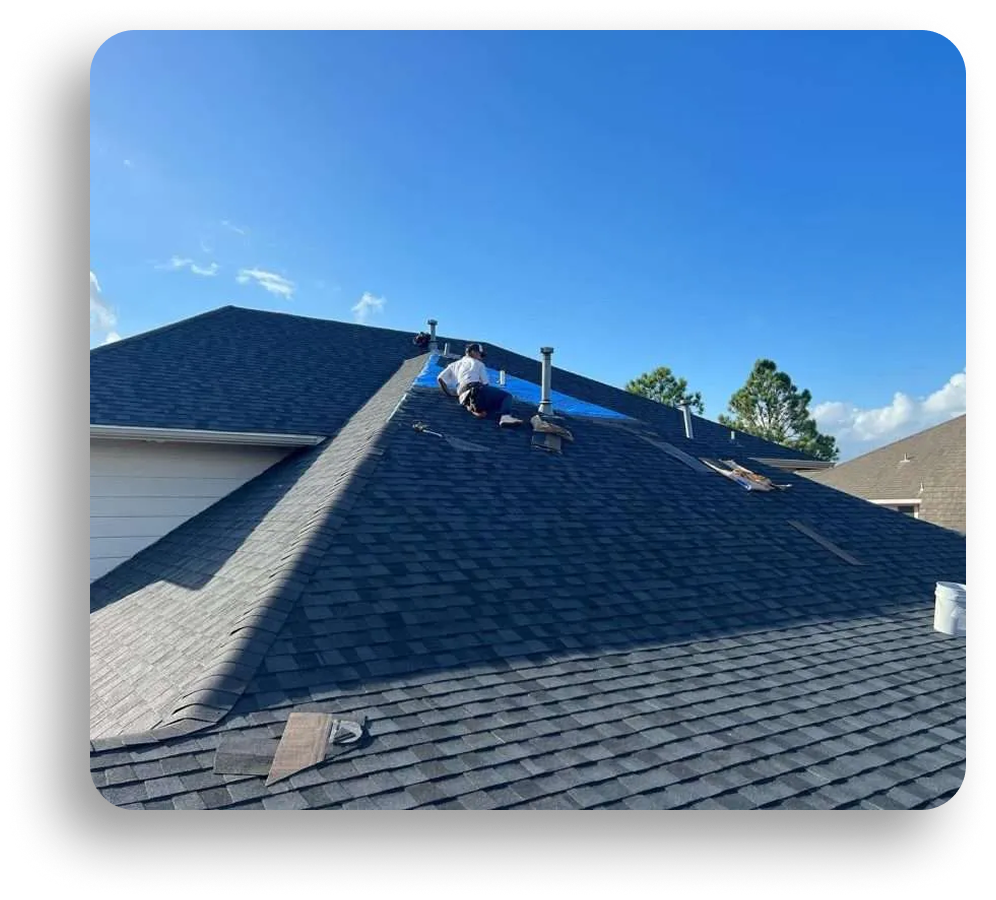 A person is working on the roof of a house under a clear blue sky, with roofing materials and tools scattered nearby, showcasing expert Residential Roofing and Roofing Repair techniques.