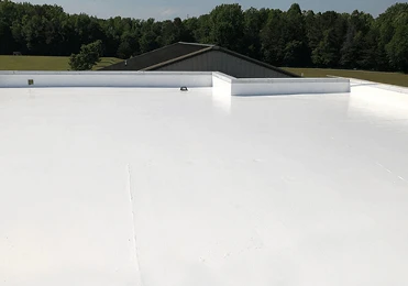 Flat white roofing surface with raised edges, likely a commercial or industrial building in North Texas, surrounded by trees and greenery under a clear sky—showcasing roofing repair quality in the region.