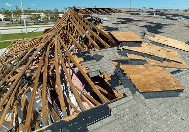 A building’s roof in North Texas with large sections missing shingles and plywood, exposing damaged wooden beams and insulation underneath—damage likely caused by a storm—may require expert roofing repair from American Patriot Roofing.