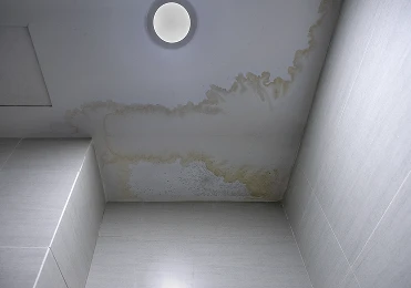 Stained bathroom ceiling with visible water damage, including yellowish-brown marks spreading from a central area near a ceiling light fixture—likely in need of Roofing Repair from American Patriot Roofing in North Texas.