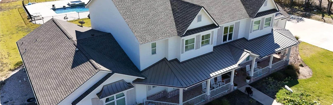 Aerial view of a large two-story house with gray shingles, white siding, and a landscaped yard. This standout in residential roofing also features a front porch, swimming pool, and inviting patio area in the background.